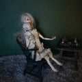 Lambwick art doll with a small lamb companion seated on a black chair against a green background.