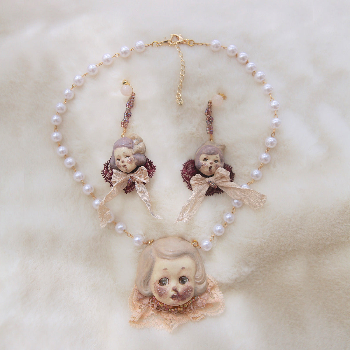 Mabel & Lucille doll-face earrings displayed with a matching doll necklace and pale beaded strand.