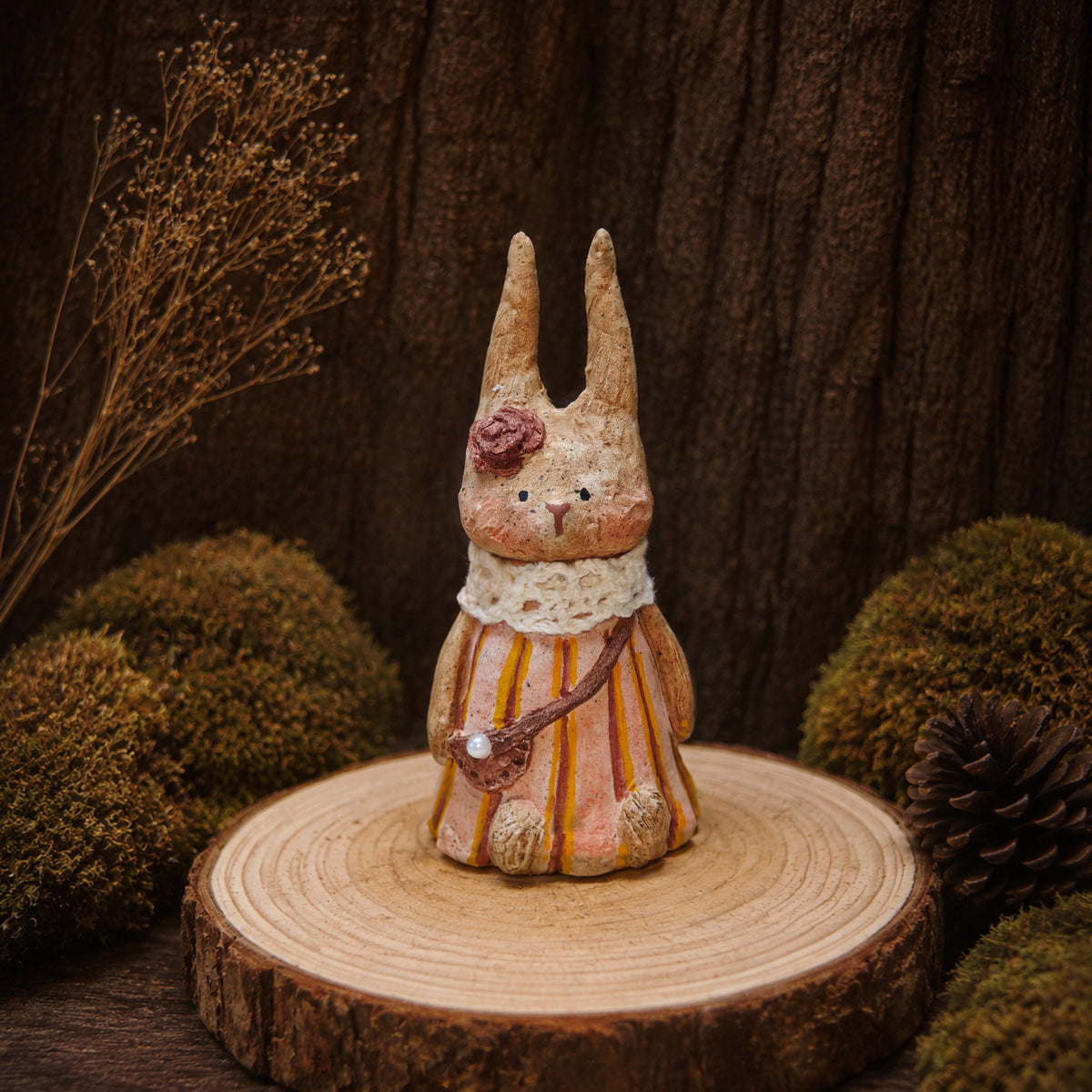 Willowwick rabbit doll wearing a pink-and-orange striped dress on a wooden base.