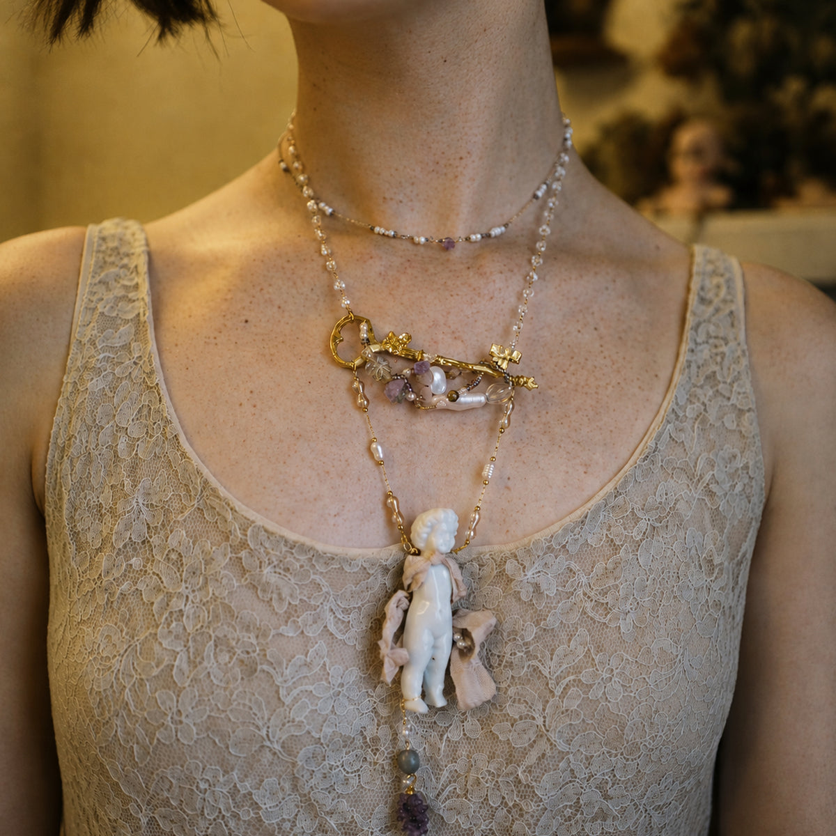 Charlotte ceramic-doll necklace worn over a pale lace top, showing its long layered design.