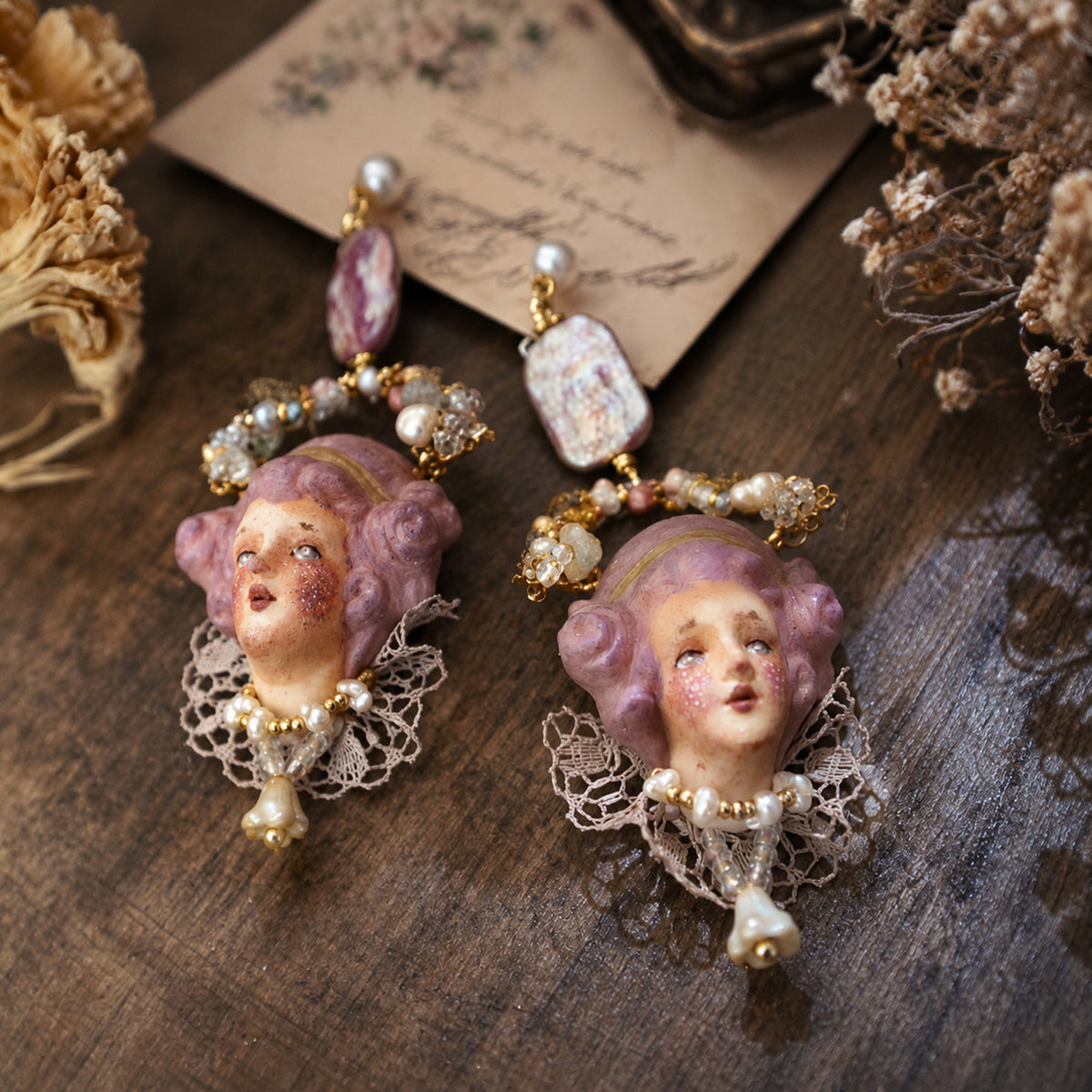 Pair of Odette doll-face earrings with lilac hair, beaded tops and hanging pearl-like drops.