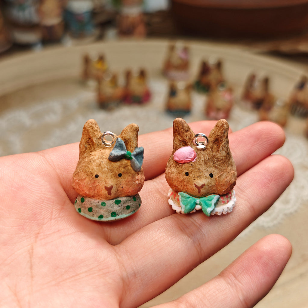 Two Winterwood rabbit pendants with teal bow details, held in a hand.