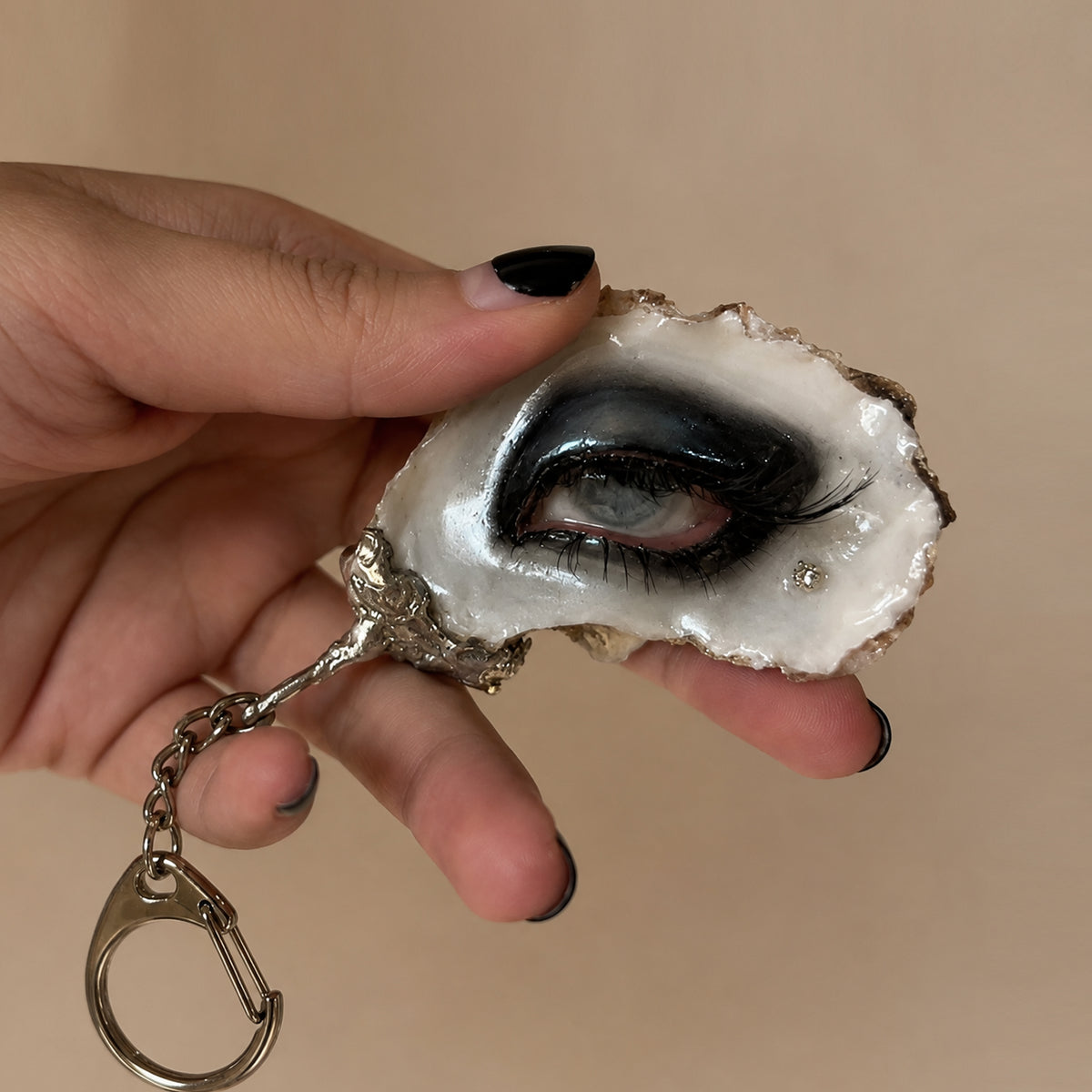 Lilith Veil Black Smoky oyster eye with a metal keychain attachment, held in a hand.