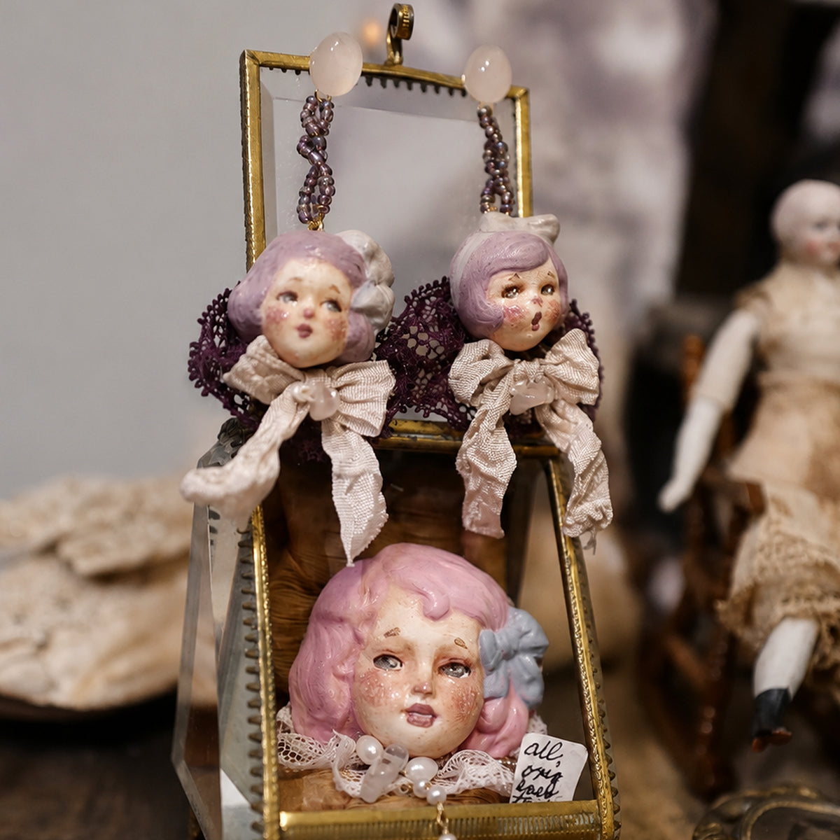 Mabel & Lucille doll earrings hanging from a small frame beside another doll-face piece.