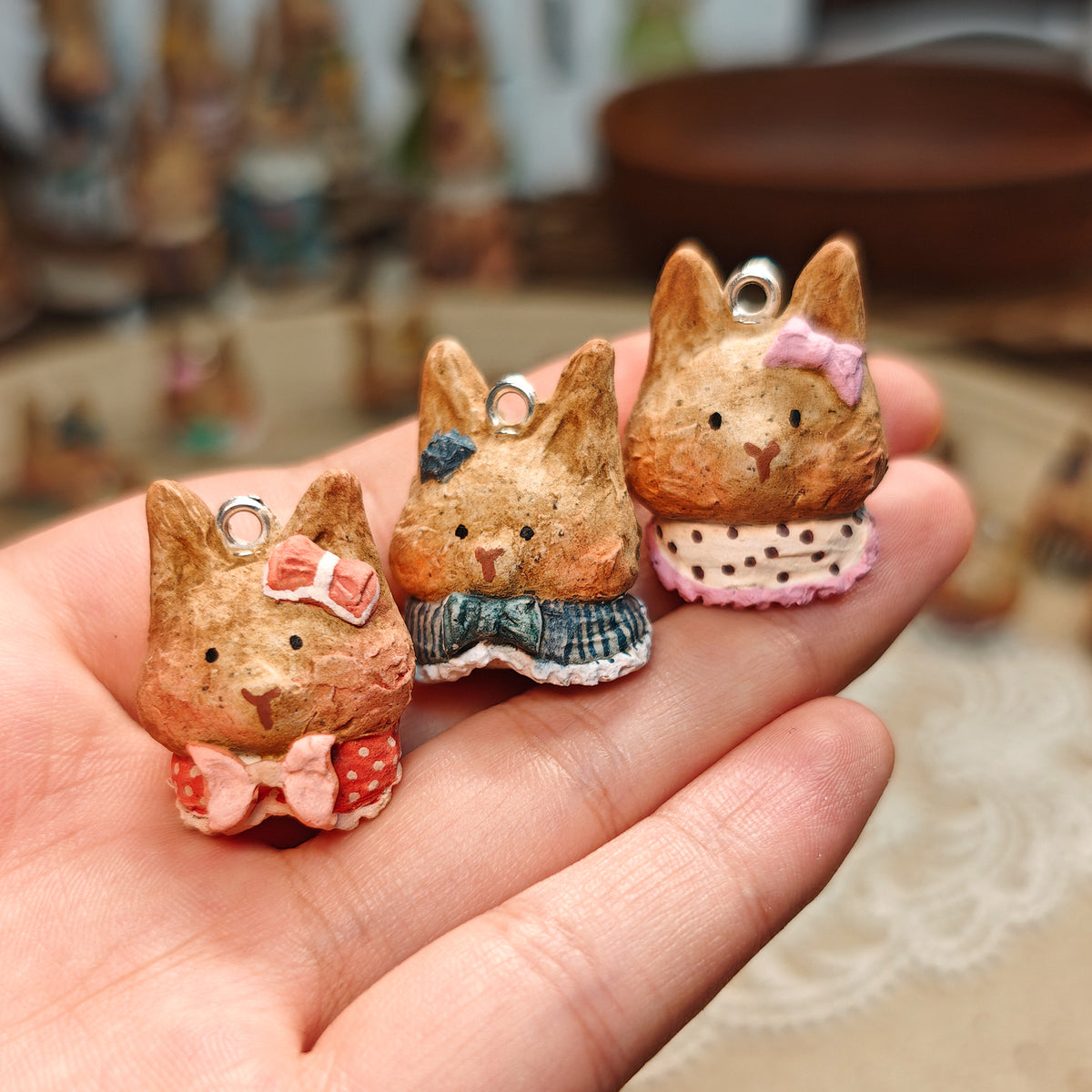 Three Winterwood rabbit pendants with pink and blue collars, held in a hand.