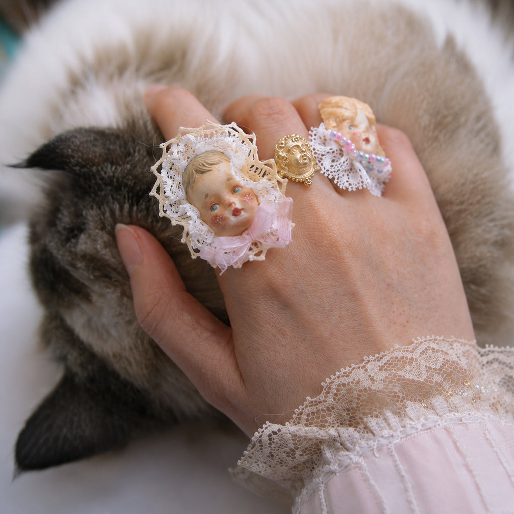 Two Lambwick doll-face rings worn together on a hand beside a resting cat.