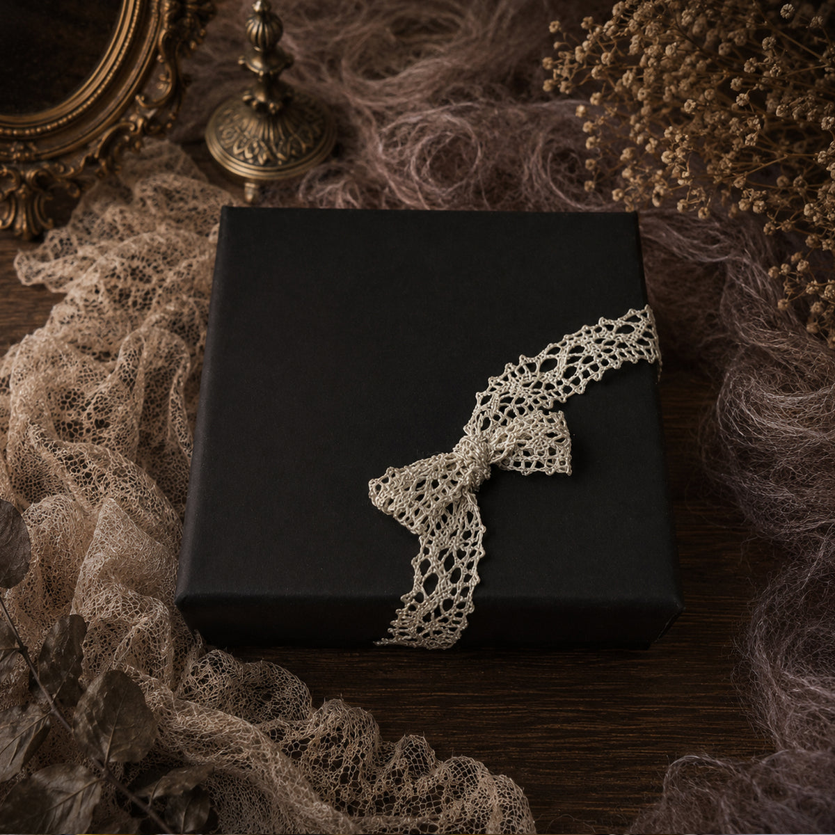 Black rectangular gift box wrapped with a cream lace band.