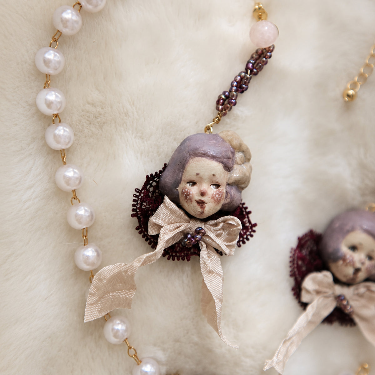 Close-up of a Mabel & Lucille doll-face earring with purple lace, pale ribbons and beaded chain.