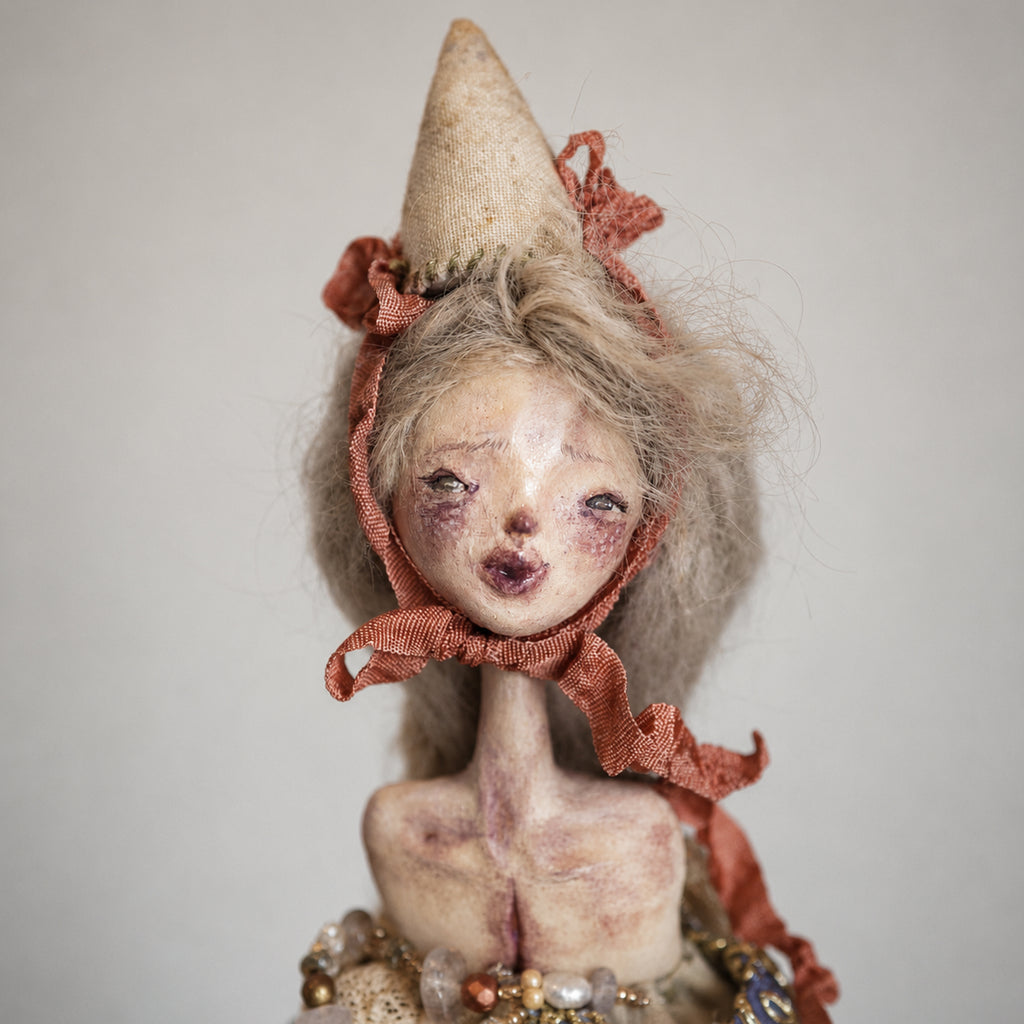 Close-up of the Lambwick hand-bell doll's face, cream cone hat and red ribbon.