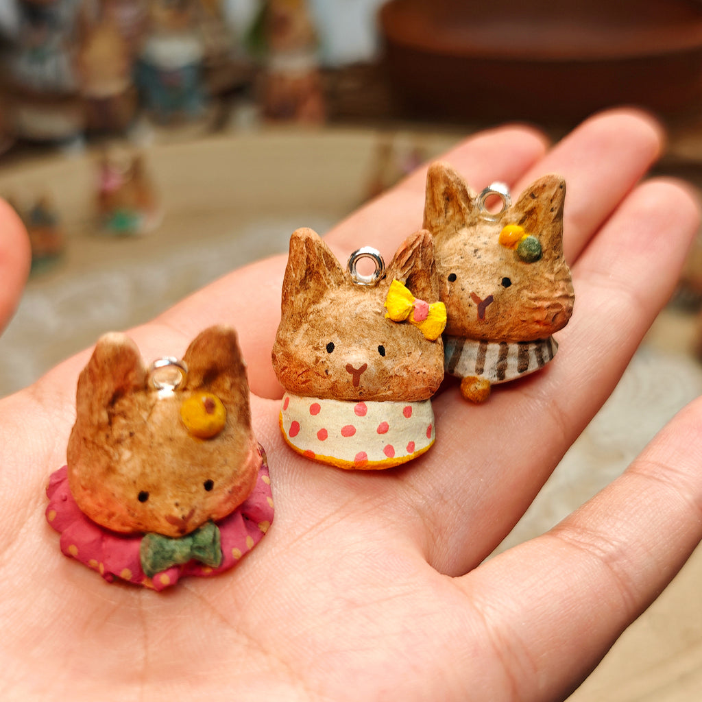 Three Winterwood rabbit pendants with red, pale and striped collars, held in a hand.