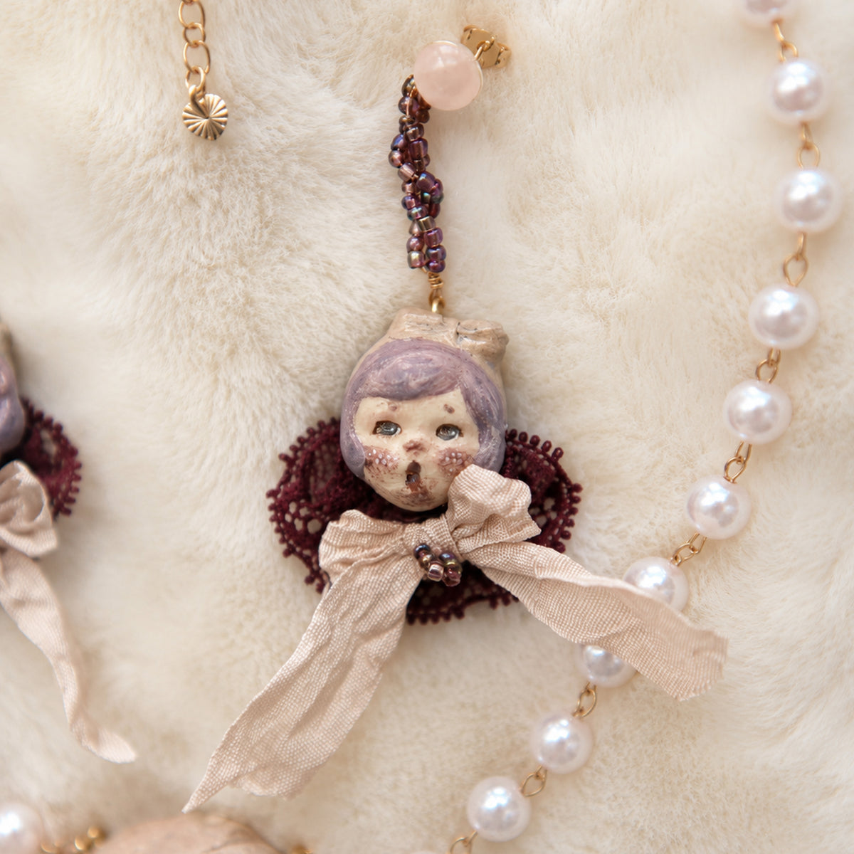 Single Mabel & Lucille doll-face earring with a pale ribbon bow and purple lace collar.