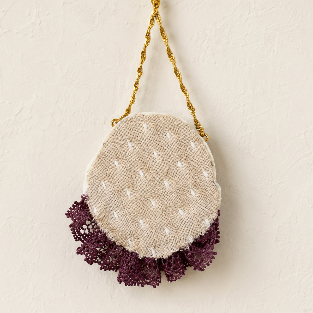 Back of a round Lambwick doll pendant showing stitched fabric and a purple lace edge.
