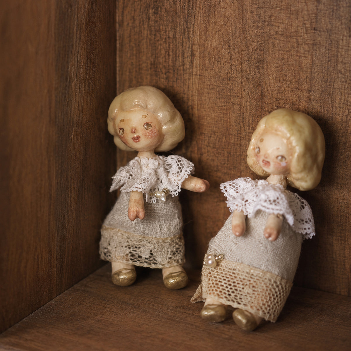 Two miniature Lambwick resident dolls standing side by side against a wooden background.