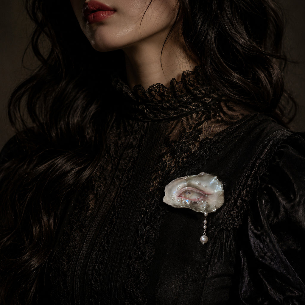 Nyra Lamb Gaze shell-eye brooch worn on a black lace top.