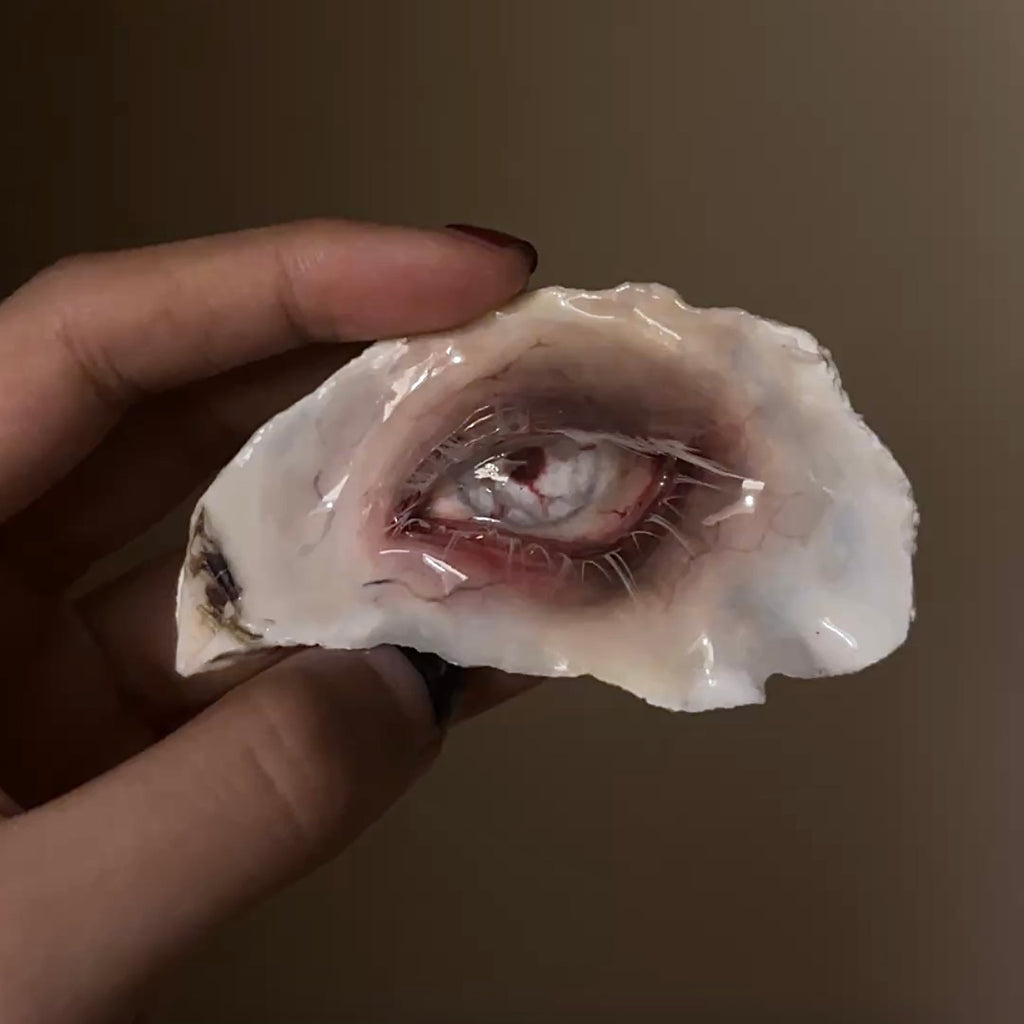 Lilith Scarlet Wound oyster eye held against a dark background, showing its red rim and pale lashes.