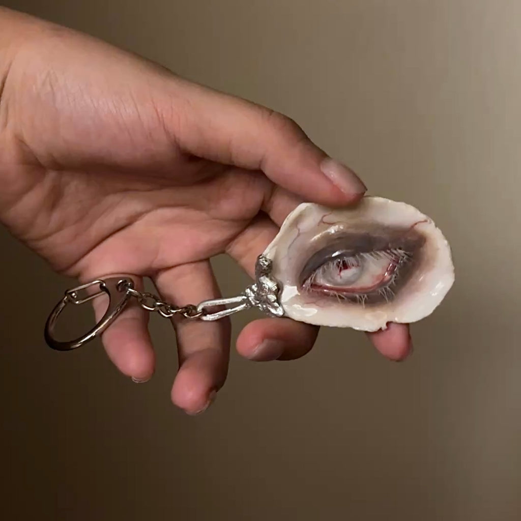 Lilith Scarlet Wound oyster eye with a metal keychain attachment, held in a hand.