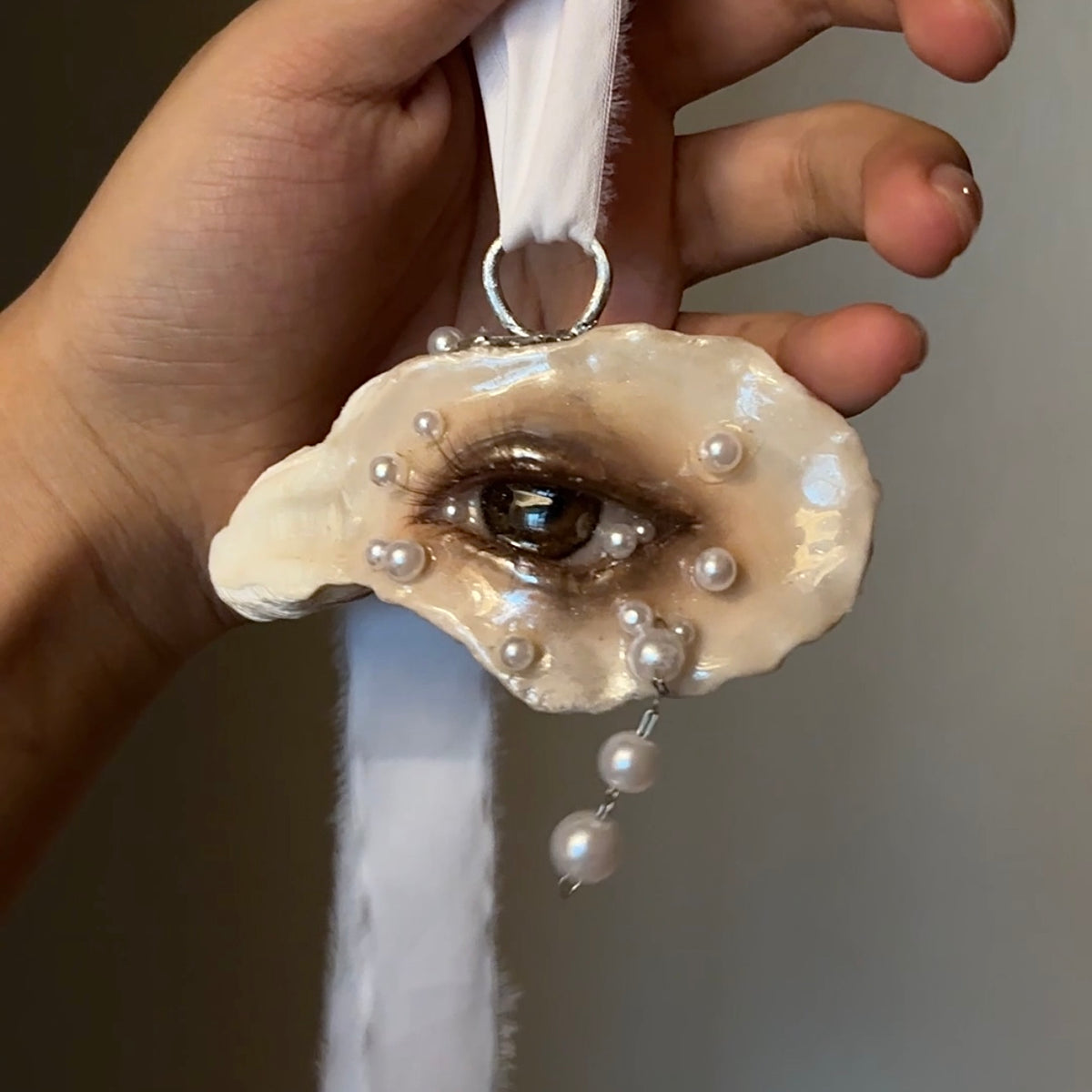 Lilith Veil: Mourning Pearl oyster eye suspended from pale ribbon, with two hanging pearl-like drops.