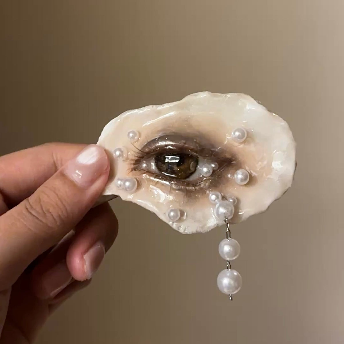 Lilith Veil: Mourning Pearl oyster eye held in a hand, showing smoky makeup and pearl-like accents.