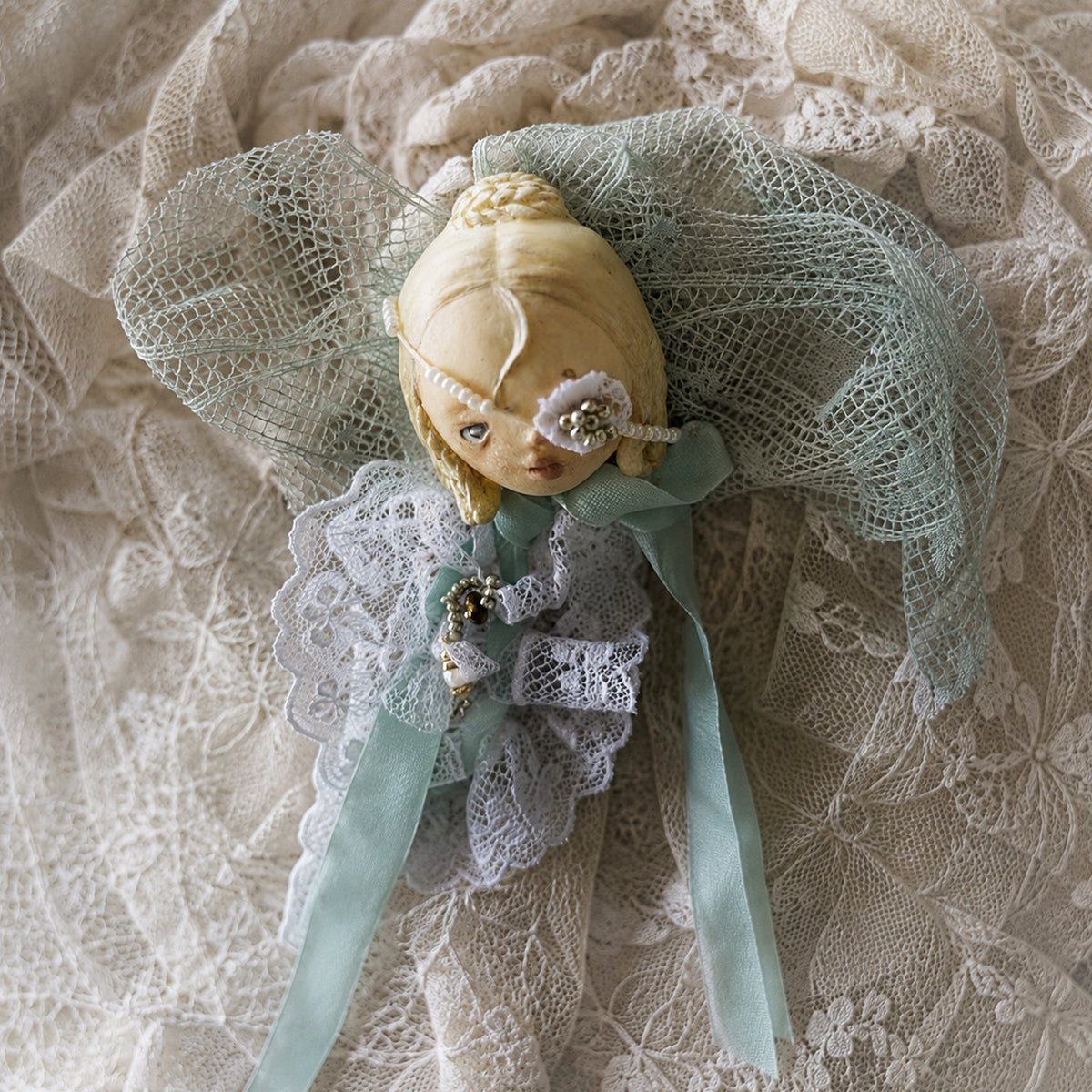 Close-up of the white-lace masked Lambwick doll brooch and mint-colored bow.