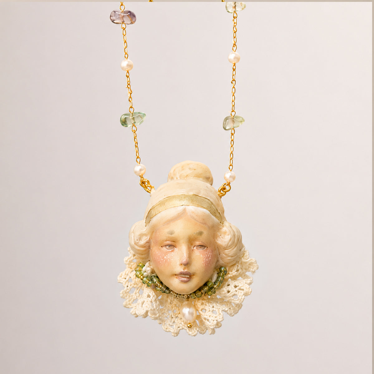 Blonde bun-haired Lambwick doll-face pendant with a pale lace collar and gold-tone chain.