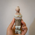 Lambwick Twin Series doll brooch with pale blue ribbons, held upright in a hand.