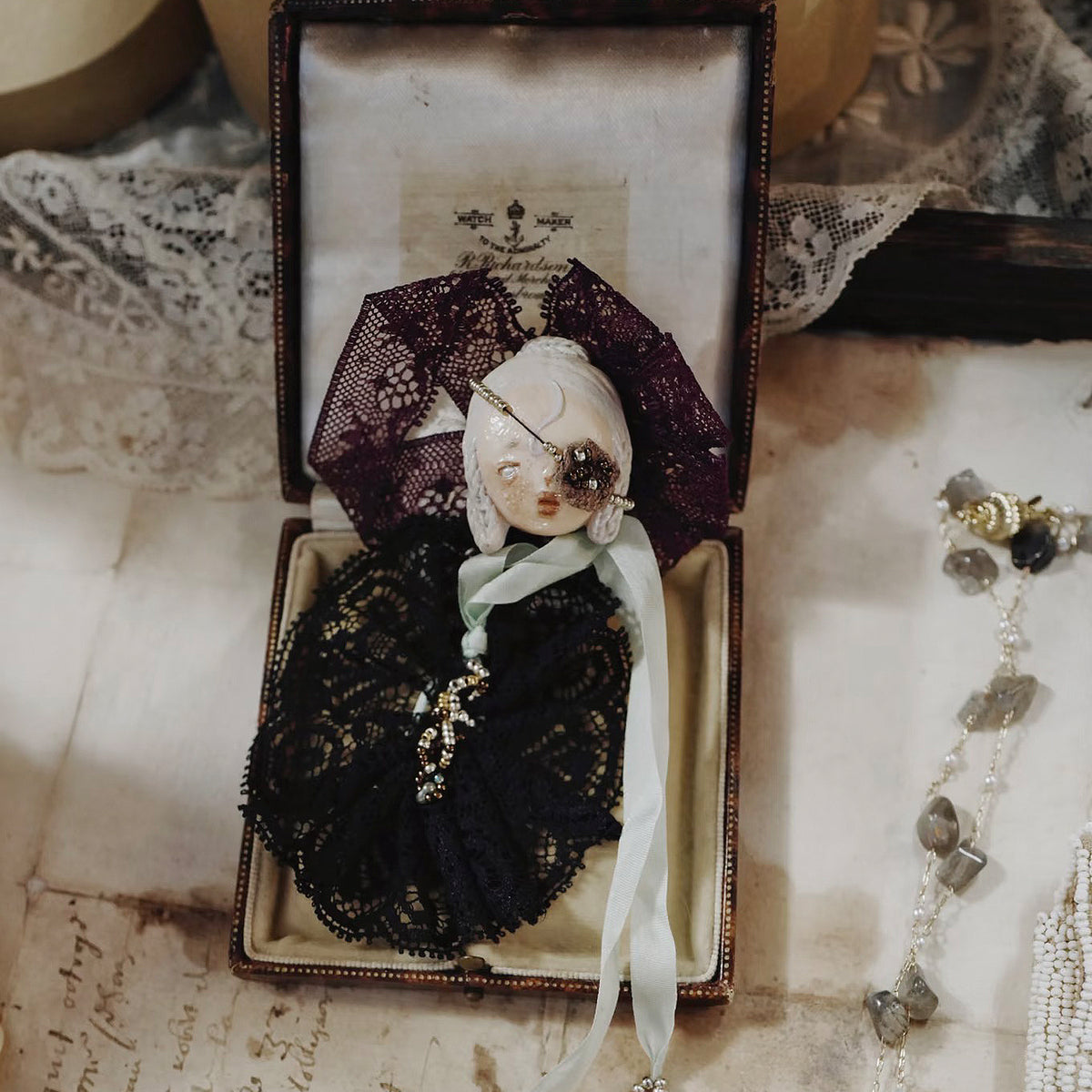 Black-lace masked Lambwick doll brooch displayed inside an open box.