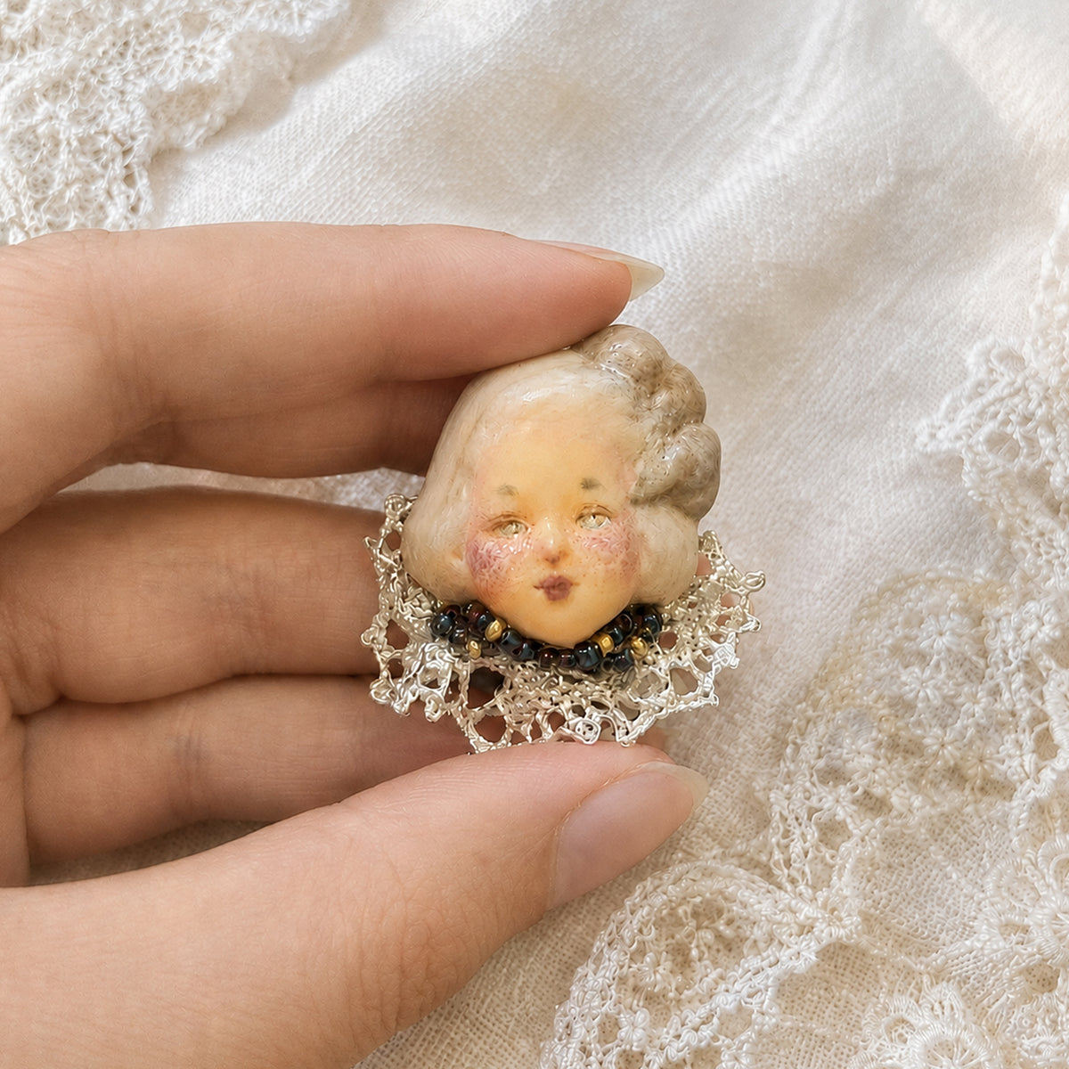 Lambwick doll ring with blonde side braids, rosy cheeks and a lace collar, held in a hand.