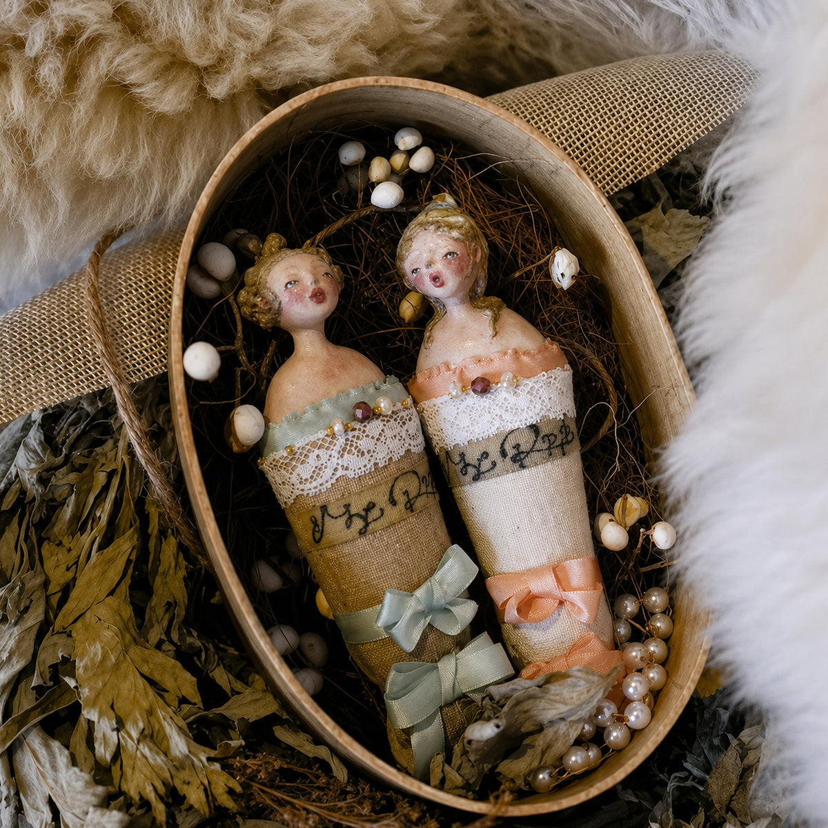 Blue- and pink-ribbon Lambwick Twin Series doll brooches inside an oval presentation box.