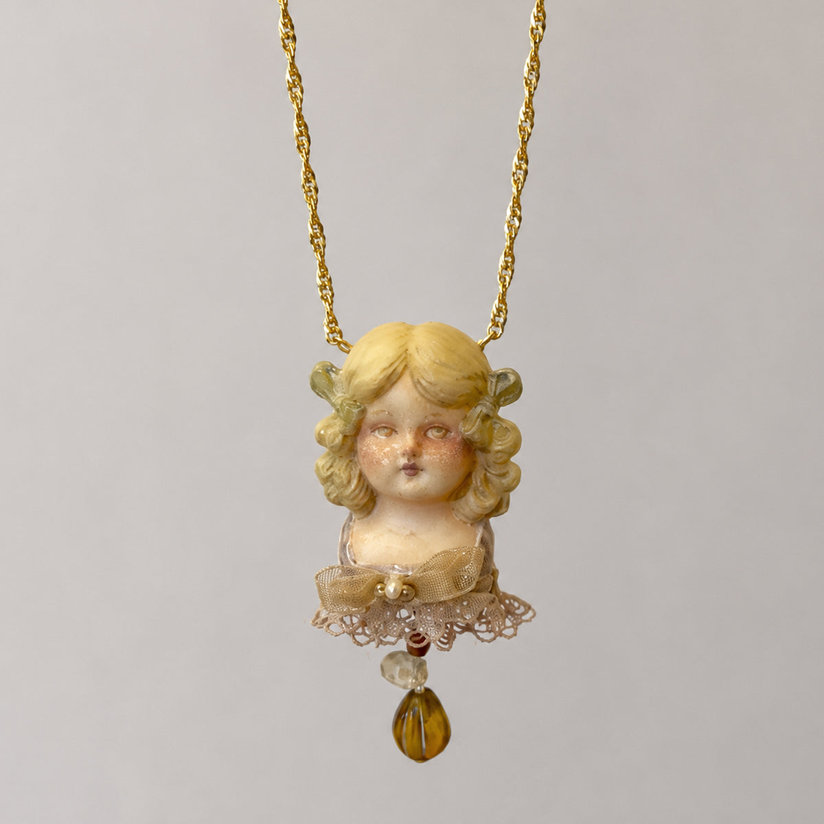 Curly-haired Lambwick doll-face pendant with a lace collar and amber-colored teardrop.