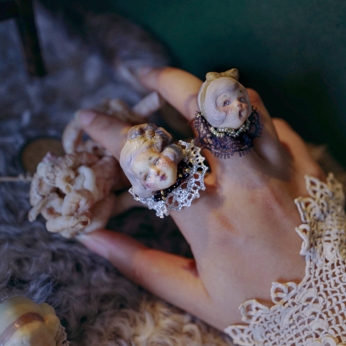 Three Lambwick doll rings worn together on a lace-covered hand.