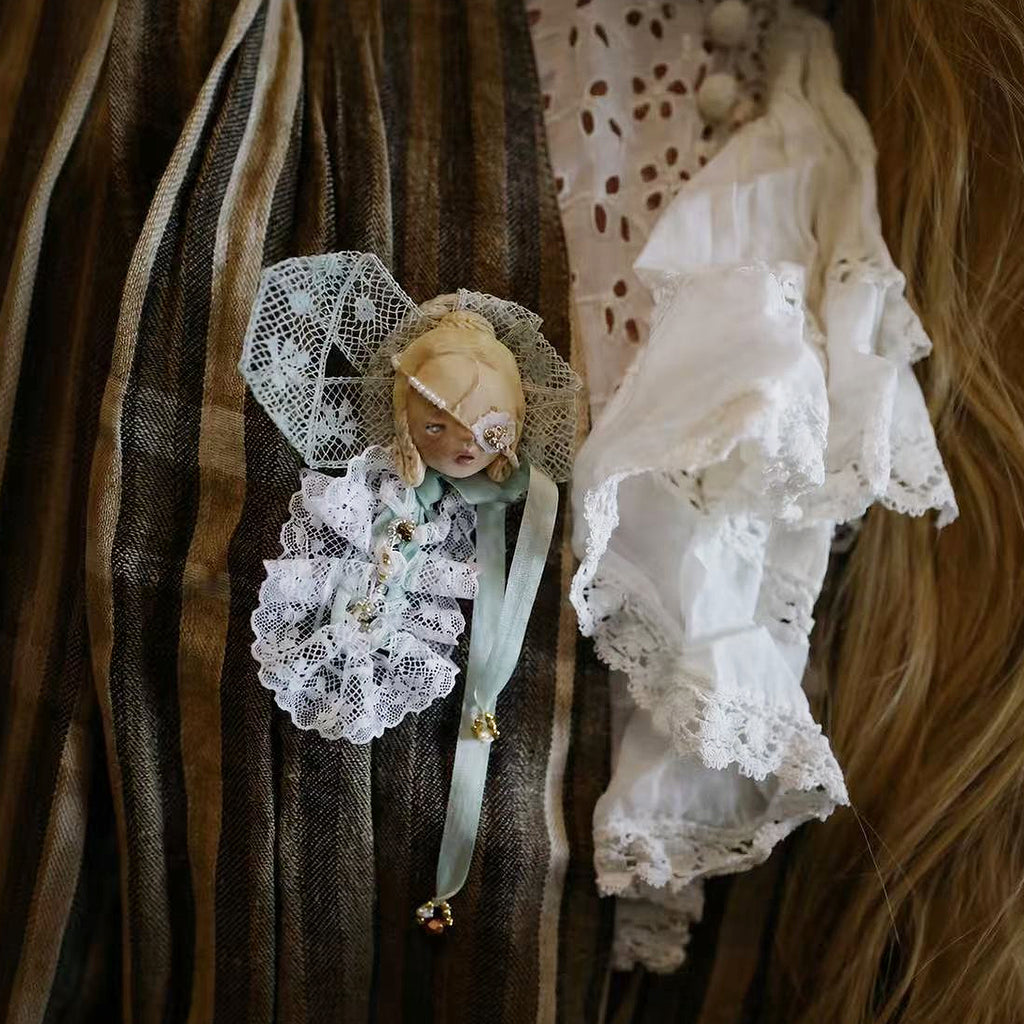 White-lace masked Lambwick doll brooch pinned to striped fabric.