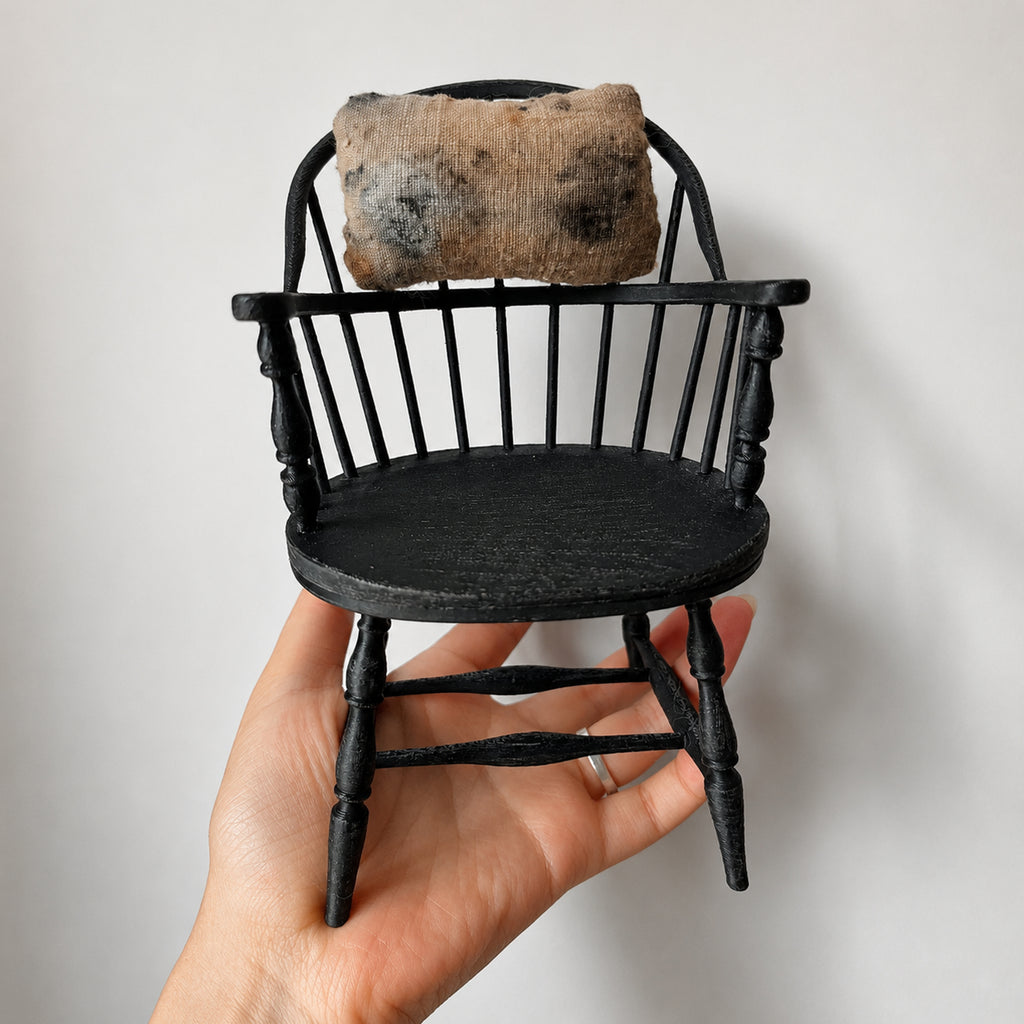 Black chair with a small patterned cushion for the Lambwick art doll, held in a hand.