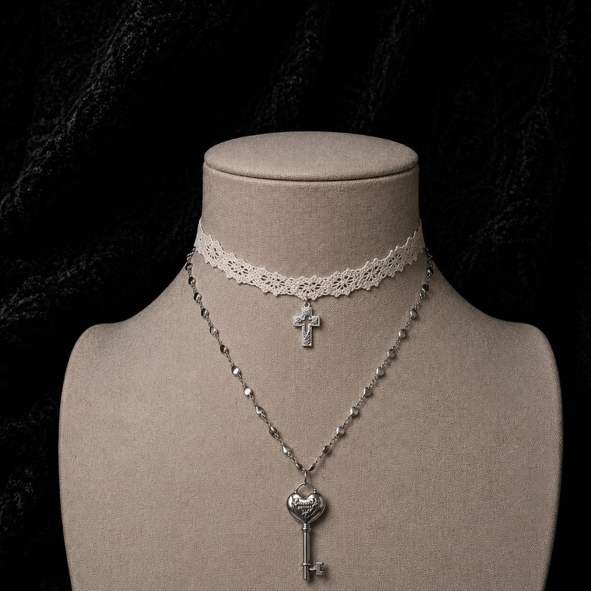 Ivory lace cross choker and heart-key necklace displayed together on a jewelry bust.