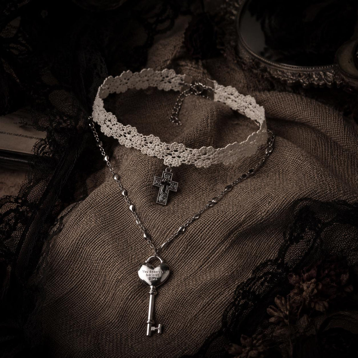 Ivory lace cross choker and heart-key necklace arranged on brown lace.