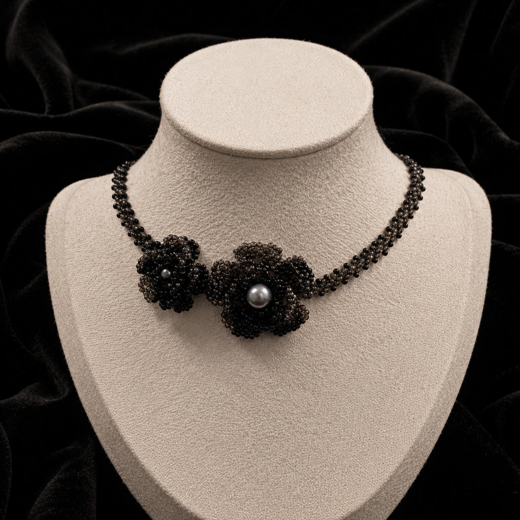 Black beaded necklace with a floral centerpiece and pale center bead on a jewelry bust.