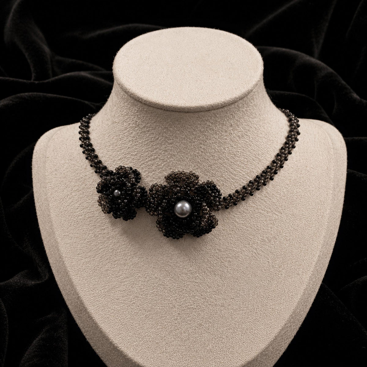 Black beaded necklace with a floral centerpiece and pale center bead on a jewelry bust.