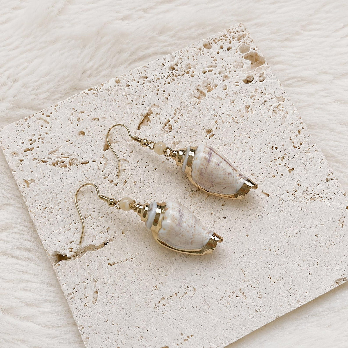 Pointed natural shell earrings with gold-tone caps arranged on cream lace.