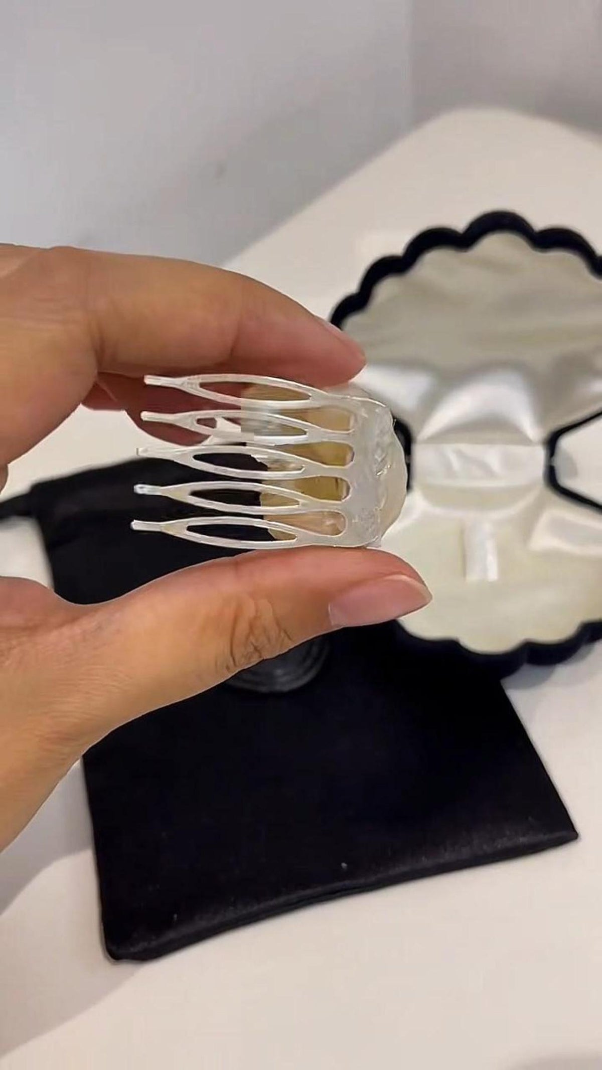 Back of a conch-shell hair comb held in a hand above its packaging.