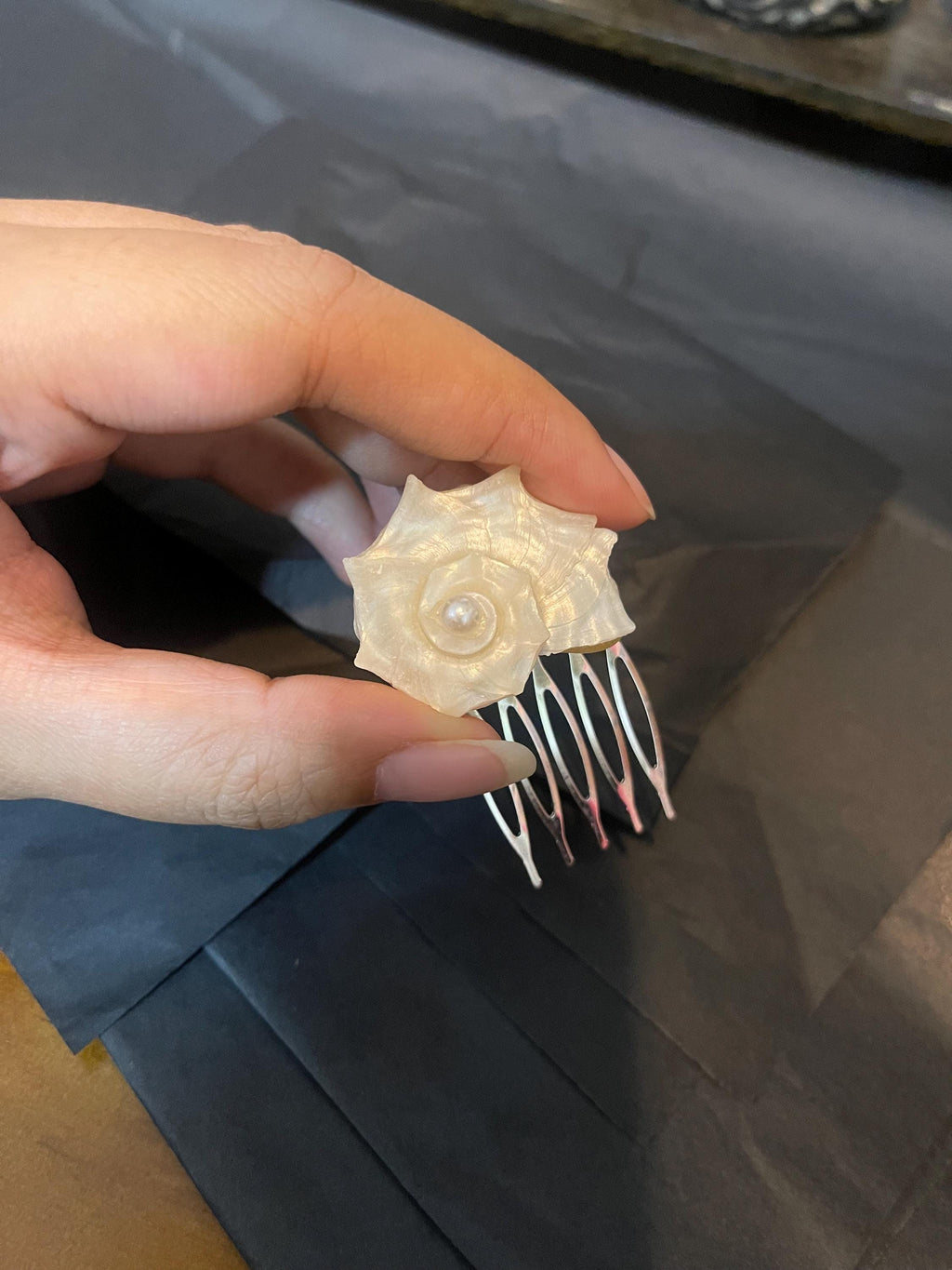 Conch-shell hair comb held in a hand to show its spiral shell and metal teeth.