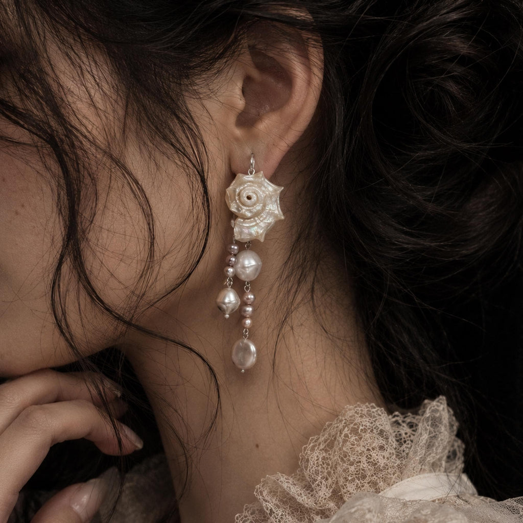 Long conch-shell earring with multiple pale bead drops shown worn beside lace.