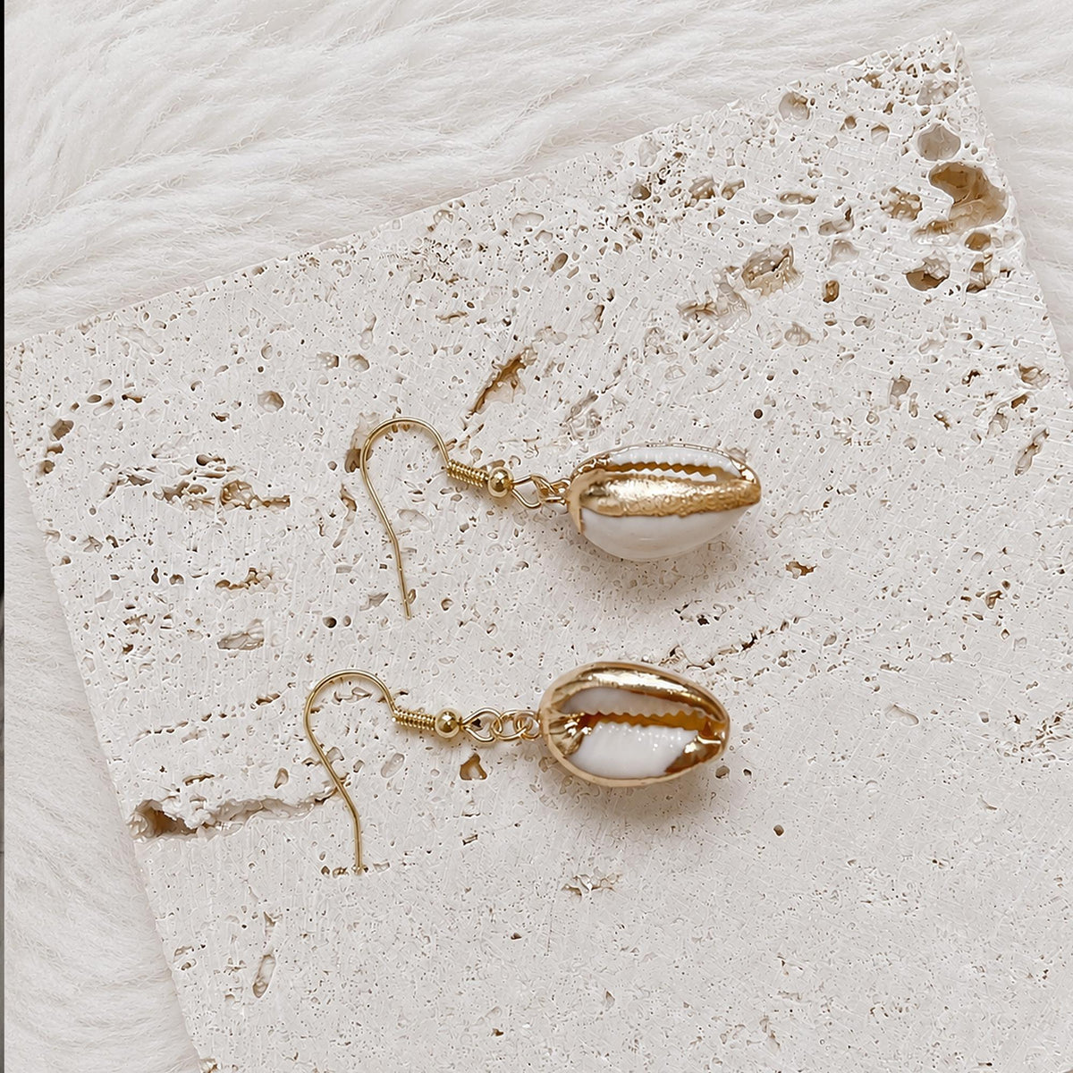 Pair of pale cowrie-shell earrings with gold-tone rims and natural slit openings.