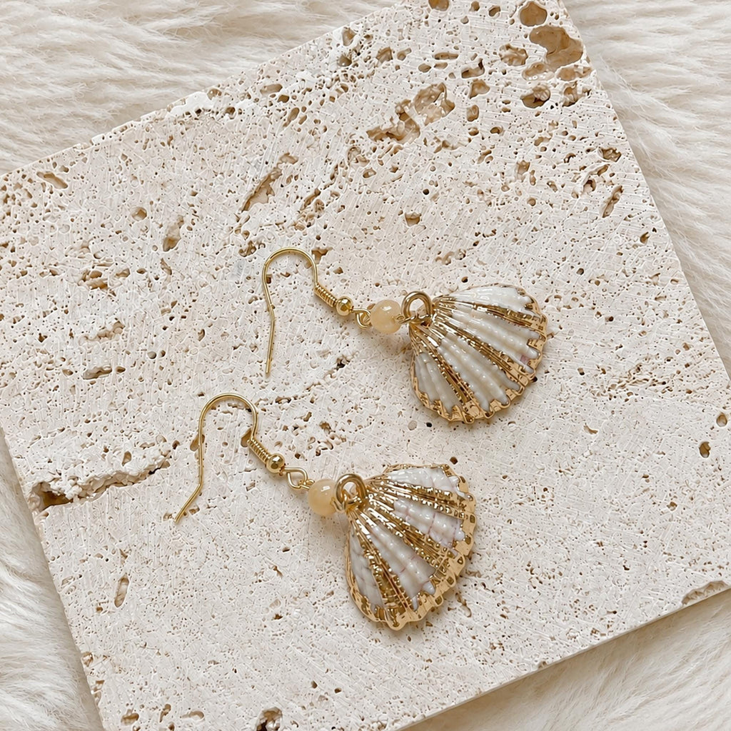 Pair of fan-shaped shell earrings with gold-tone edges arranged on cream lace.