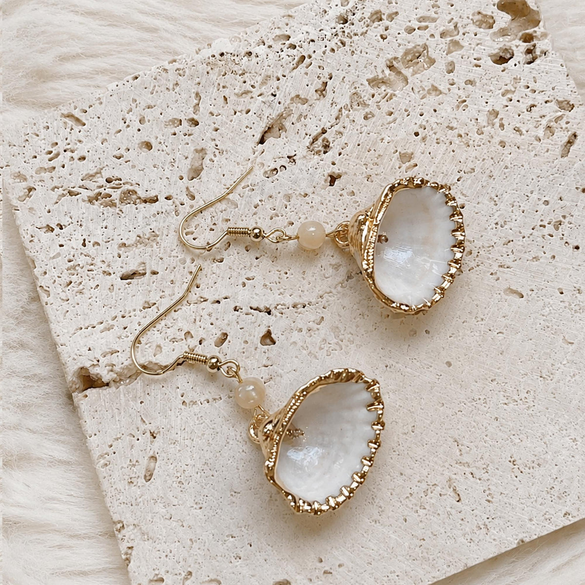 Reverse view of fan-shaped shell earrings showing pale interiors and gold-tone edges.