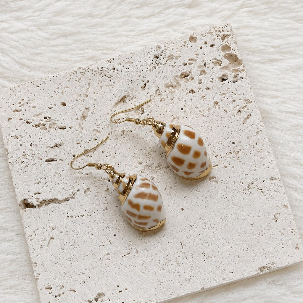 Pair of spotted cowrie-shell drop earrings arranged on cream lace.