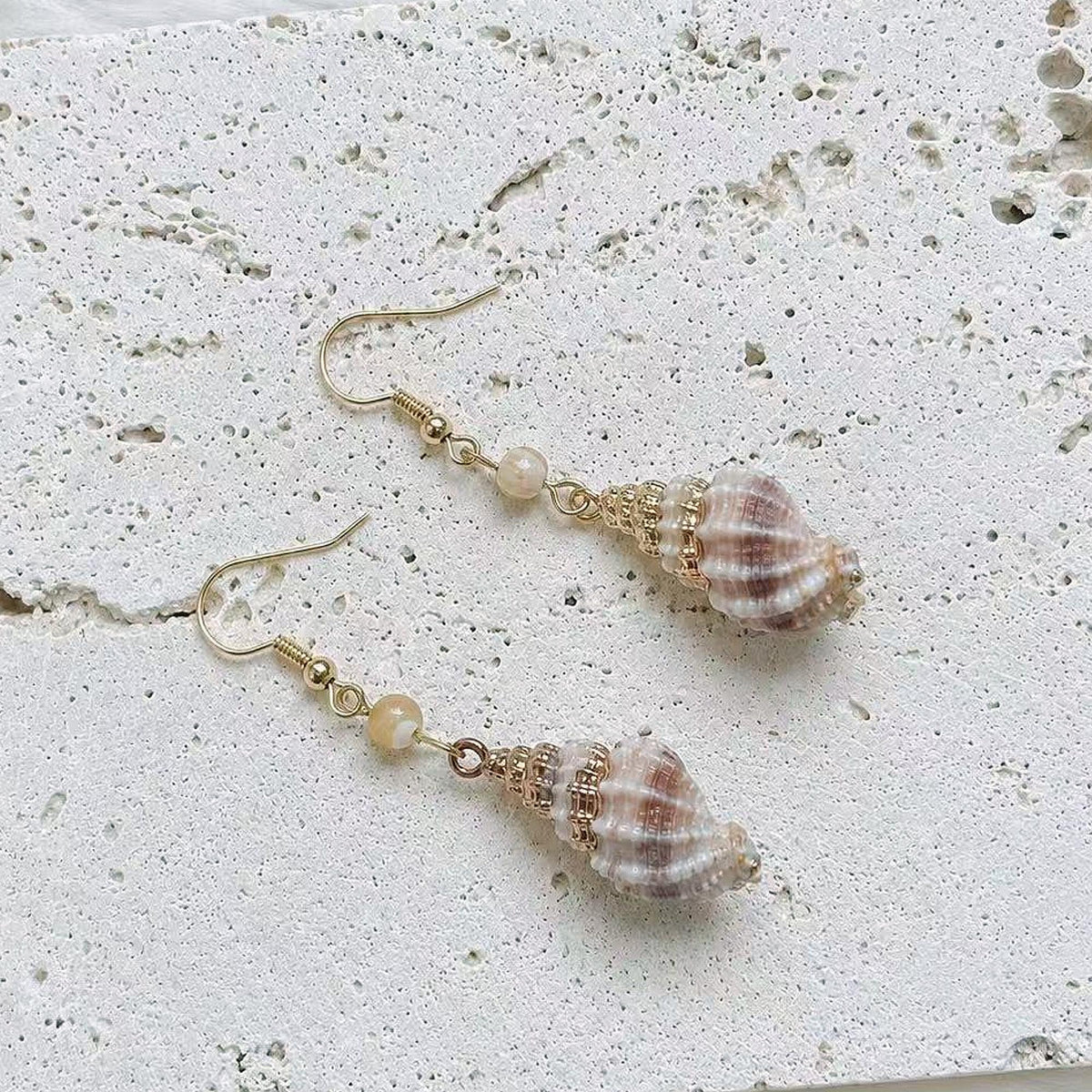 Pair of rounded striped shell earrings with pale bead accents and gold-tone hooks.