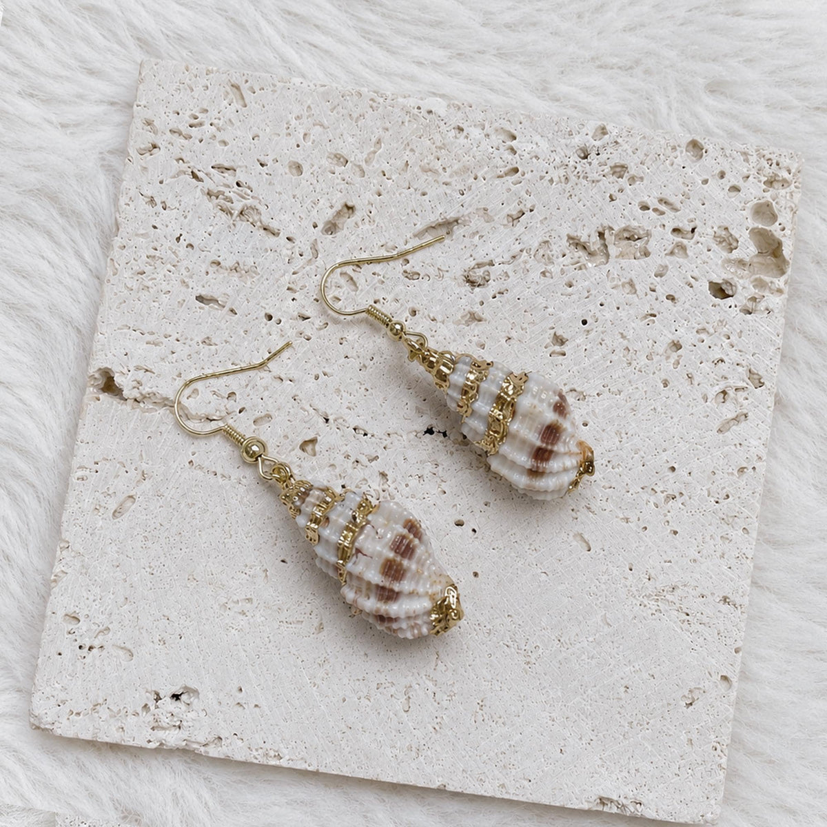 Angled close view of striped conch-shell earrings with gold-tone caps.