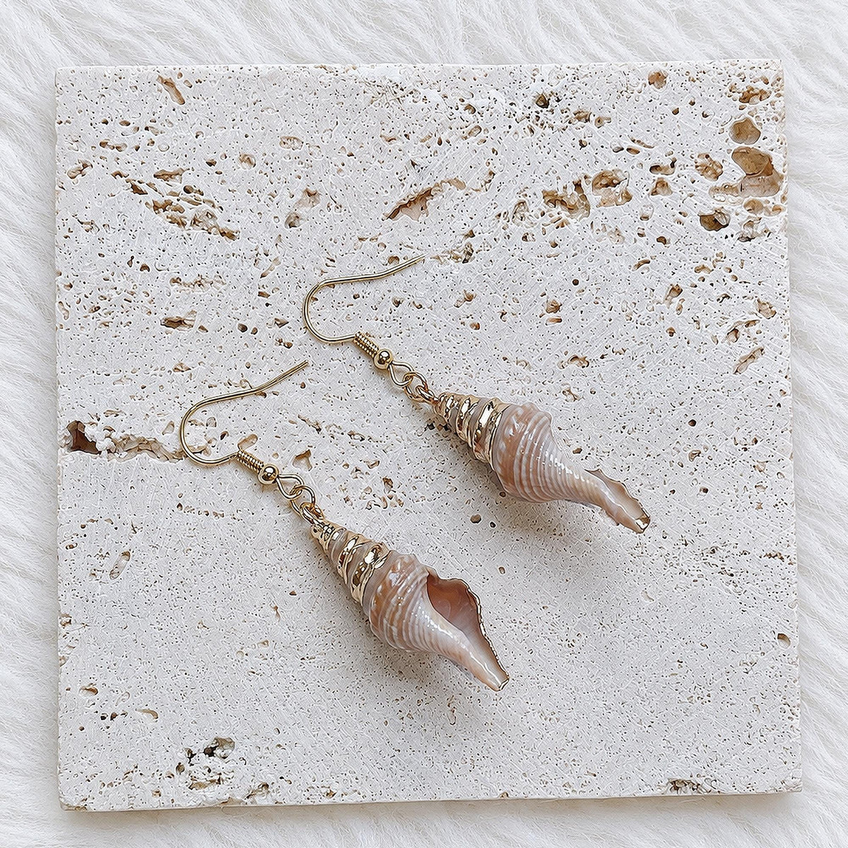 Pair of pointed spiked conch-shell earrings on cream lace.