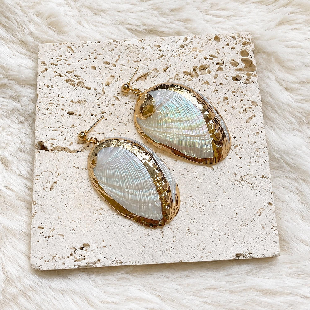 Pair of oval iridescent shell earrings with gold-tone rims on cream lace.
