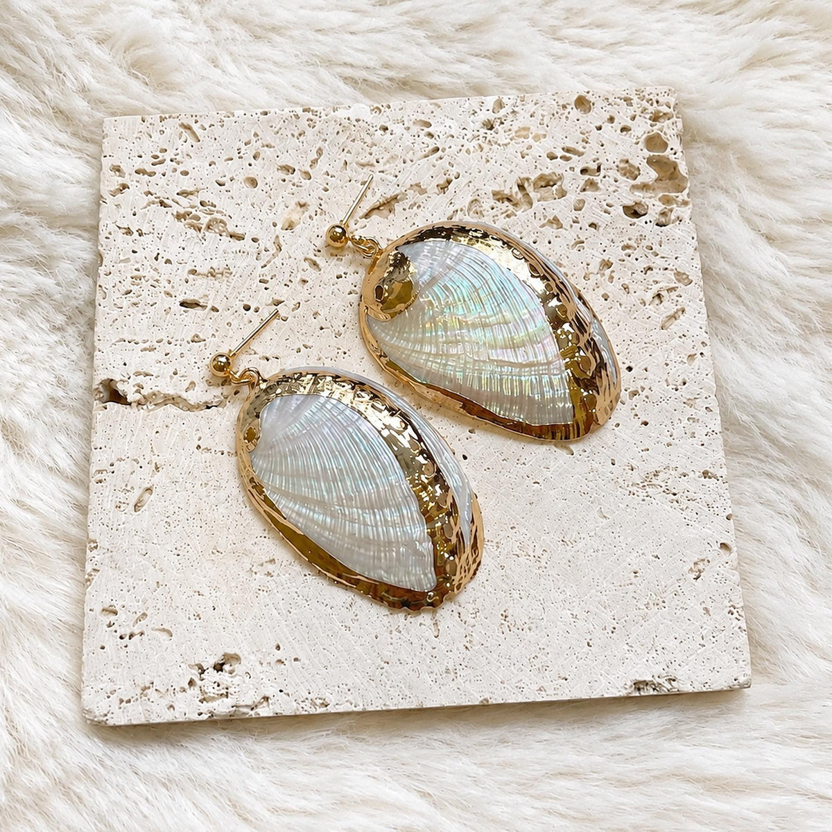 Pair of oval iridescent shell earrings with gold-tone rims on cream lace.