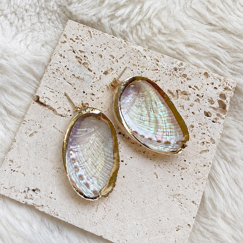 Reverse view of oval shell earrings showing their pale reflective interiors and gold-tone rims.